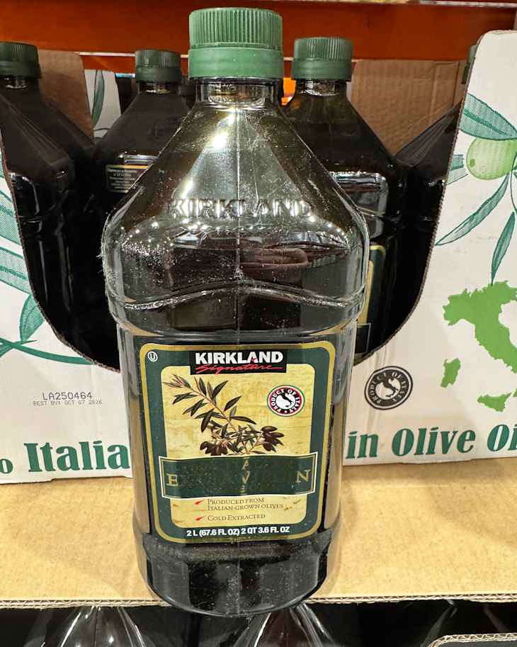 Large bottle of Kirkland Signature extra virgin olive oil with a green cap, displayed among other bottles on a shelf.
