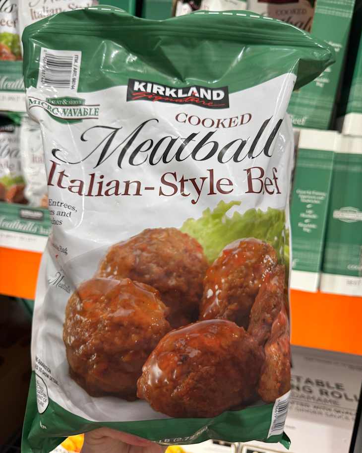Cooked Italian-style beef meatballs in a green and white bag, featuring a glossy sauce and lettuce.