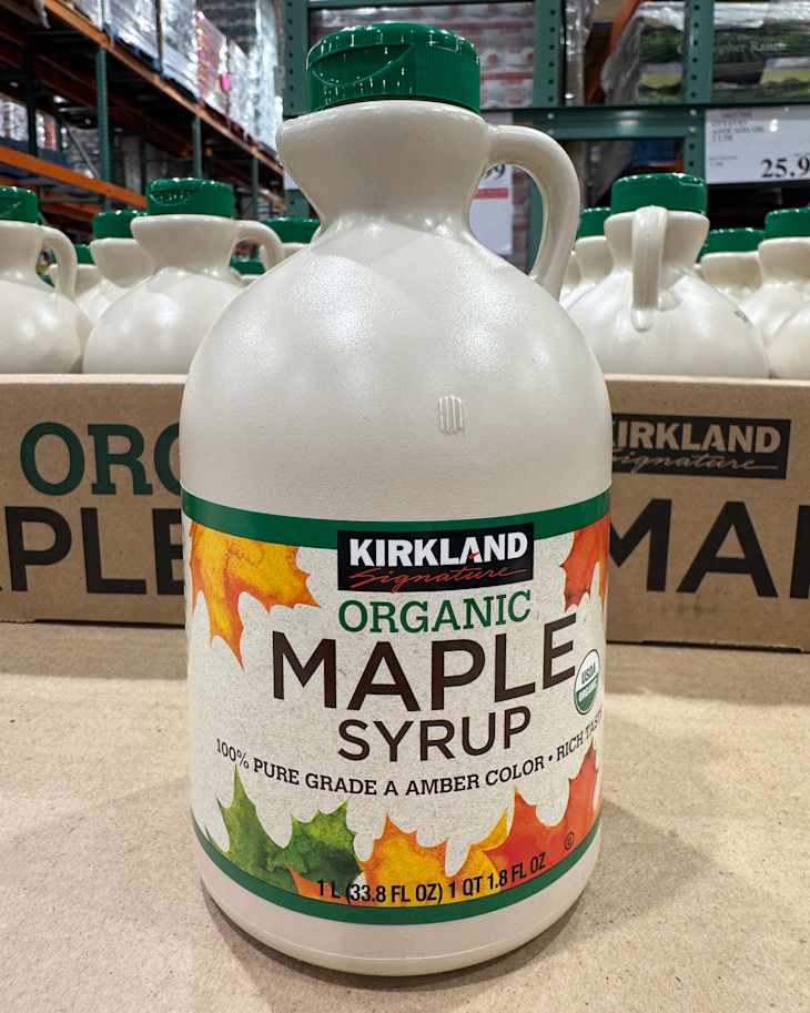 Large bottle of Kirkland organic maple syrup with colorful leaf design, displayed in a warehouse setting.