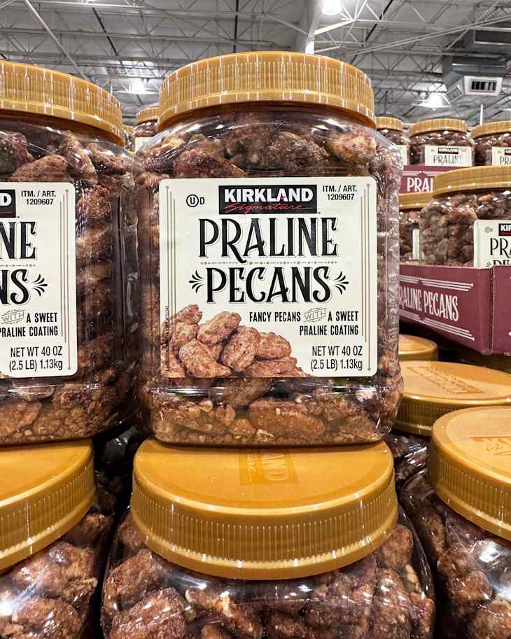 Large jars of Kirkland Praline Pecans stacked in a store, featuring a sweet praline coating.