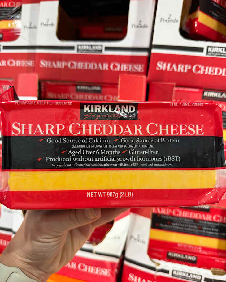 Block of Kirkland Sharp Cheddar Cheese held in hand, with red packaging and nutritional information visible.