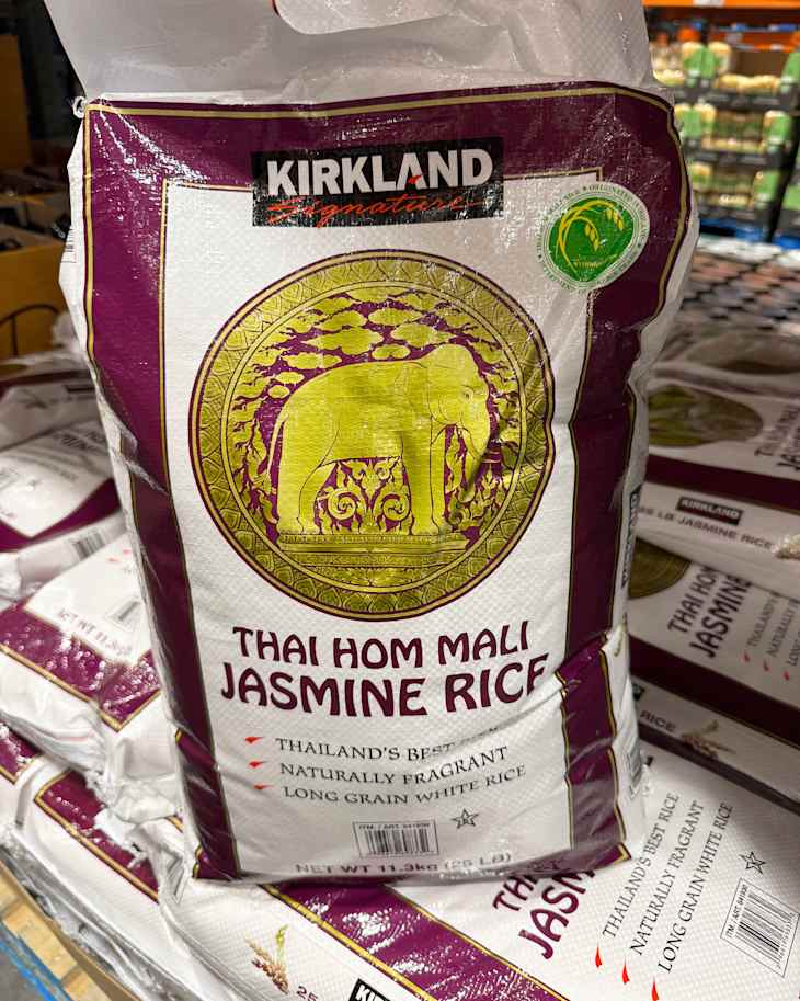 Bag of Kirkland Thai Hom Mali Jasmine Rice featuring an elephant design, stacked among other rice bags in a store.