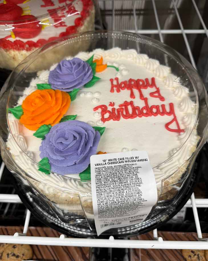 Birthday cake with white frosting, orange and purple roses, and "Happy Birthday" written in red icing.