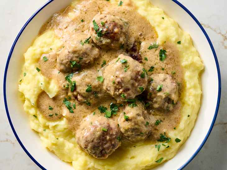 Creamy mashed potatoes topped with Swedish meatballs in gravy, garnished with parsley.