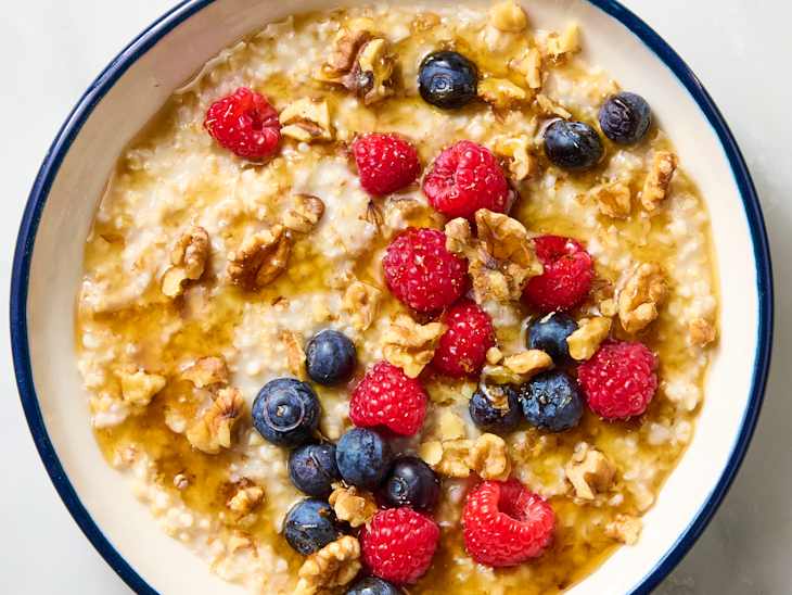 Bowl of oatmeal topped with raspberries, blueberries, walnuts, and a drizzle of syrup.