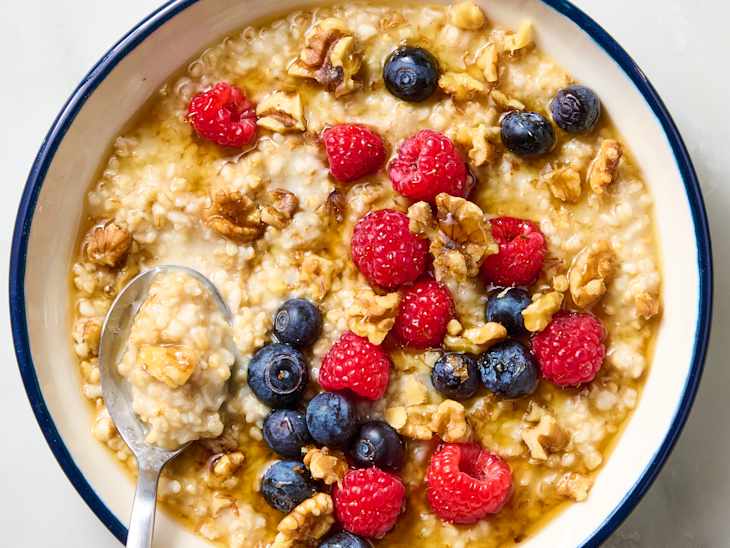 Bowl of oatmeal topped with raspberries, blueberries, walnuts, and a drizzle of syrup, with a spoon resting inside.