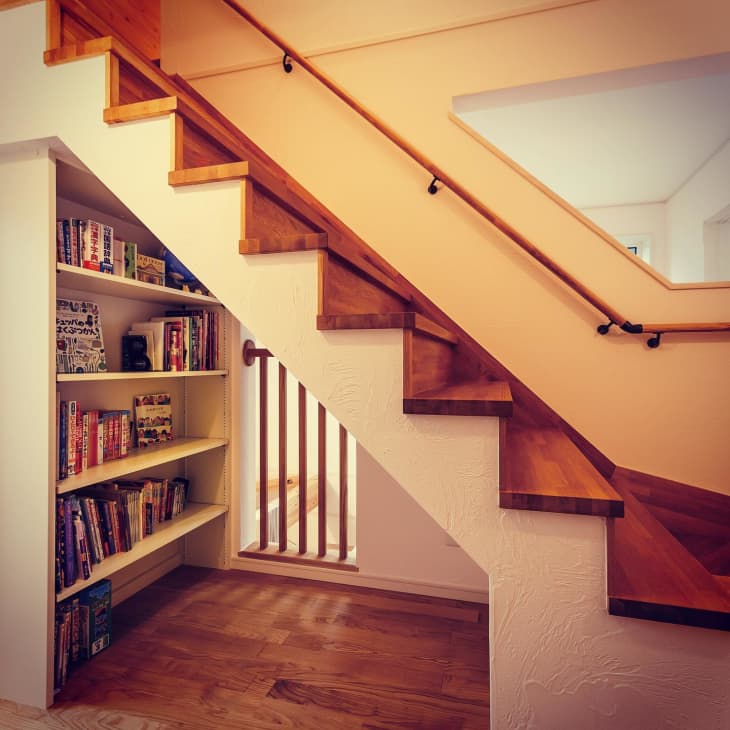 a bookcase under a wooden staircase with neutral-colored walls