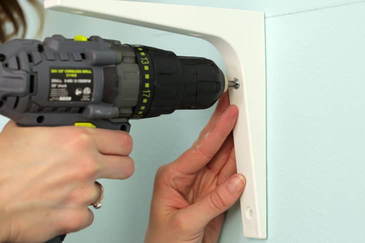 Close up of a person's hand drilling screws through wall bracket into wall