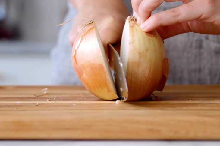 close up of hands cutting a white onion in half with a chefs knife