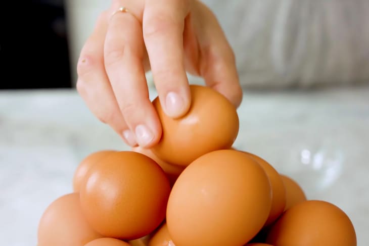 a hand picking a brown egg from the top of a pile of brown eggs