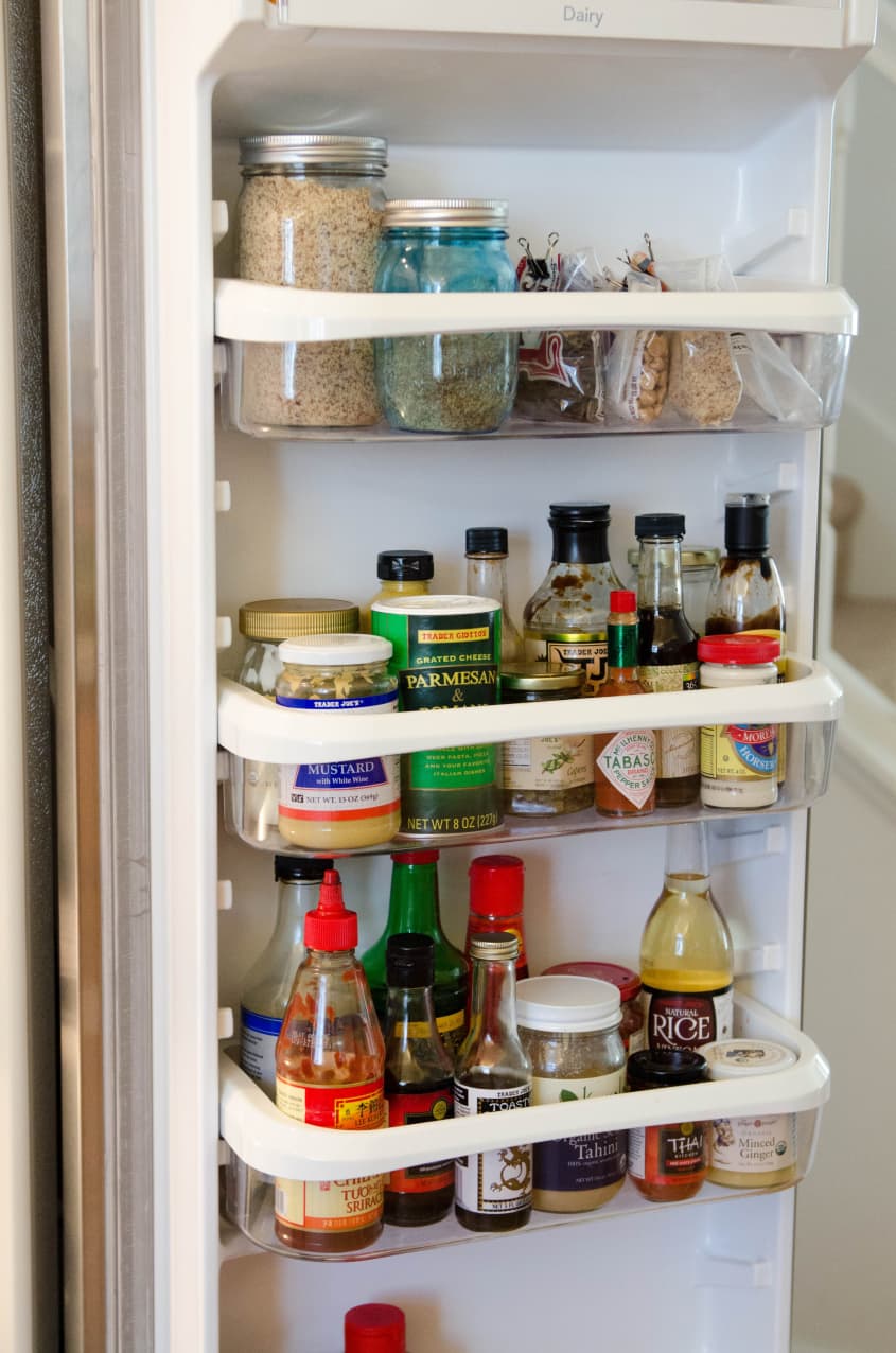 Refrigerator door shelves with jars of grains, spices, and various condiments including mustard, soy sauce, and hot sauce.