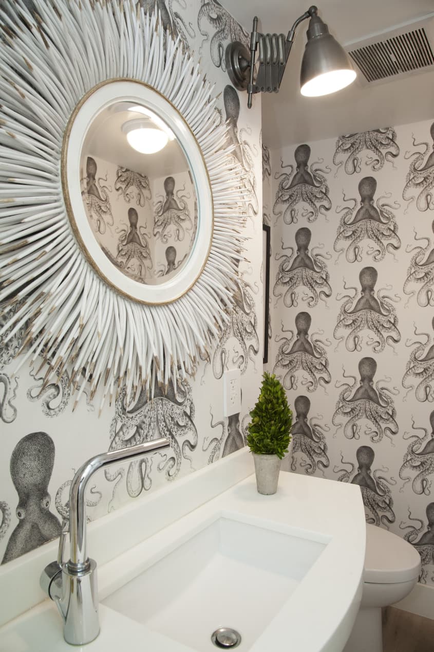 A powder room with octopus wallpaper and a sunburst mirror