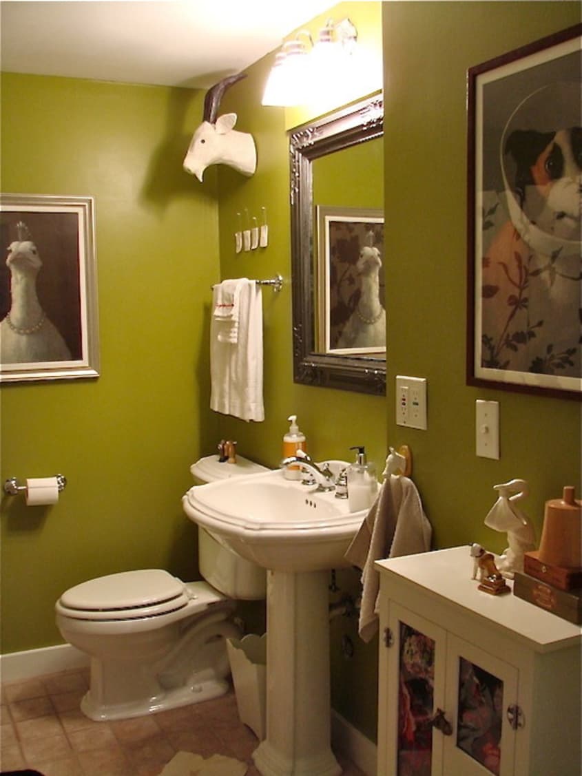 A framed mirror and framed art in a green bathroom.