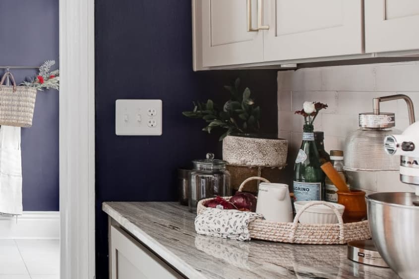A white light switch plate against a dark blue kitchen wall