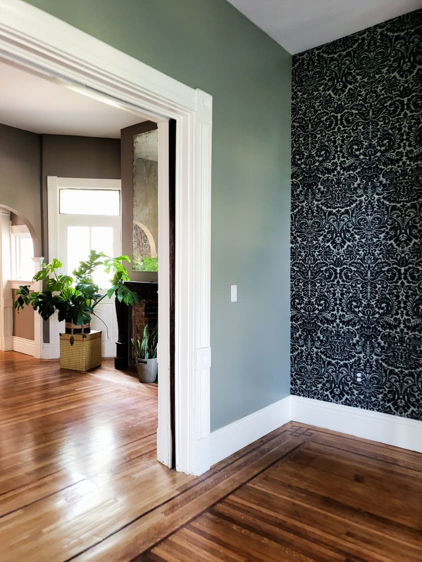 Living space with one green painted wall and one wall wallpapered with a black and white patterned paper. There is an outlet on the wallpapered wall that blends in, since it is papered to match the wall it's on.