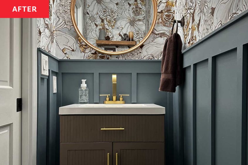 bathroom after makeover: gold framed round mirror over sink, floral illustrated wallpaper, gold hardware, deep blue walls