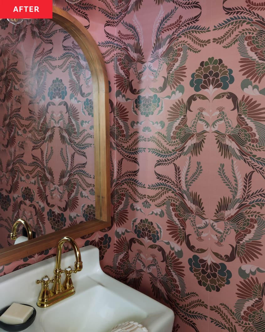 After: a pink floral wallpapered bathroom with an arched mirror over a sink with a gold faucet