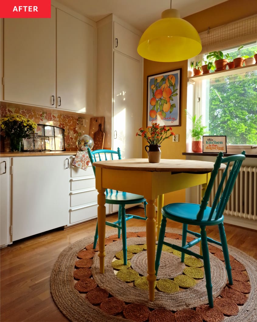 yellow walls, teal wood chairs, yellow wood table for two, plant shelf hanging in window, white radiator, yellow round lighting fixture, floral art, flowers in pitcher, round pink yellow and tan rope rug, white cabinets wall to ceiling, wood counter, wood floors, disco ball, yellow flowers, tea towel, decorative window, plants