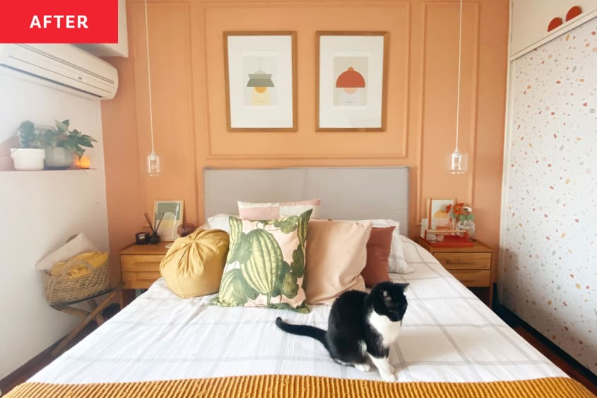 bedroom after repainting/remodel. Cantaloupe colored walls with decorative moulding, art prints of lamps, wood nightstand, white, ochre, blush, rose bedding with watermelon pattern pillow, cat on bed