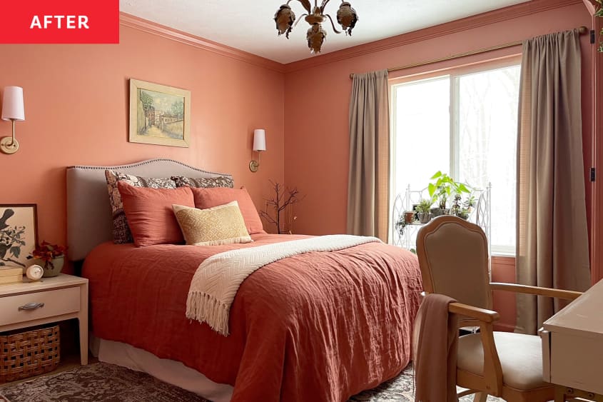 Neatly made bed with peach/rust colored bedding in color drenched bedroom with matching walls. Arm chair tucked under writing desk.