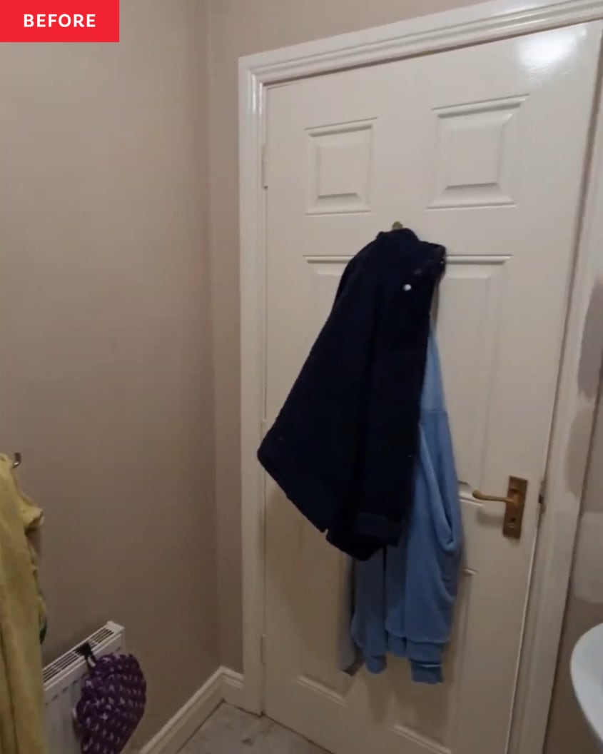 A beige bathroom with clothing hanging up on the back of a door.