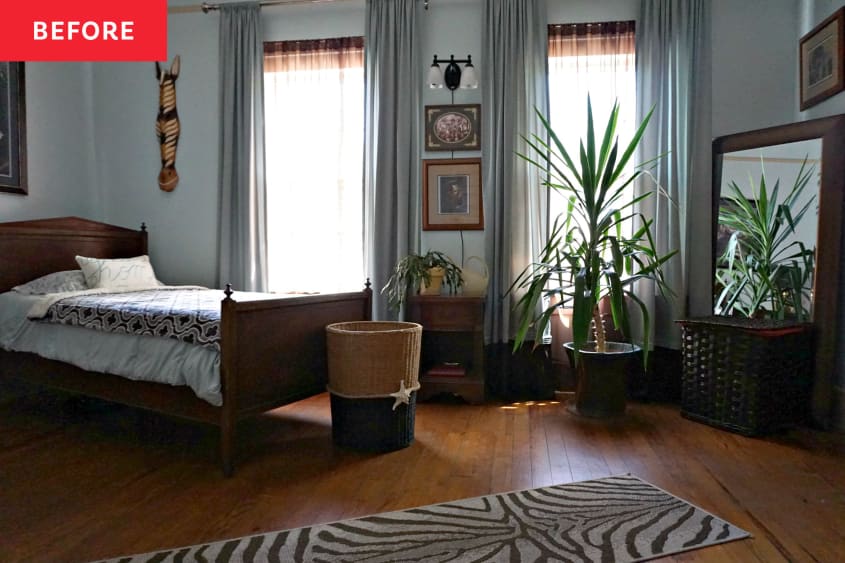 A wood floored bedroom with a bed, plant and mirror.