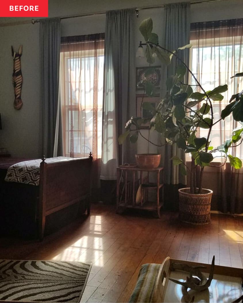 A bedroom with wooden floors, two large windows and tall growing plants.