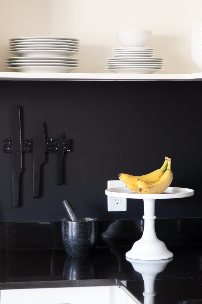 Black knives on a metallic strip in a black kitchen