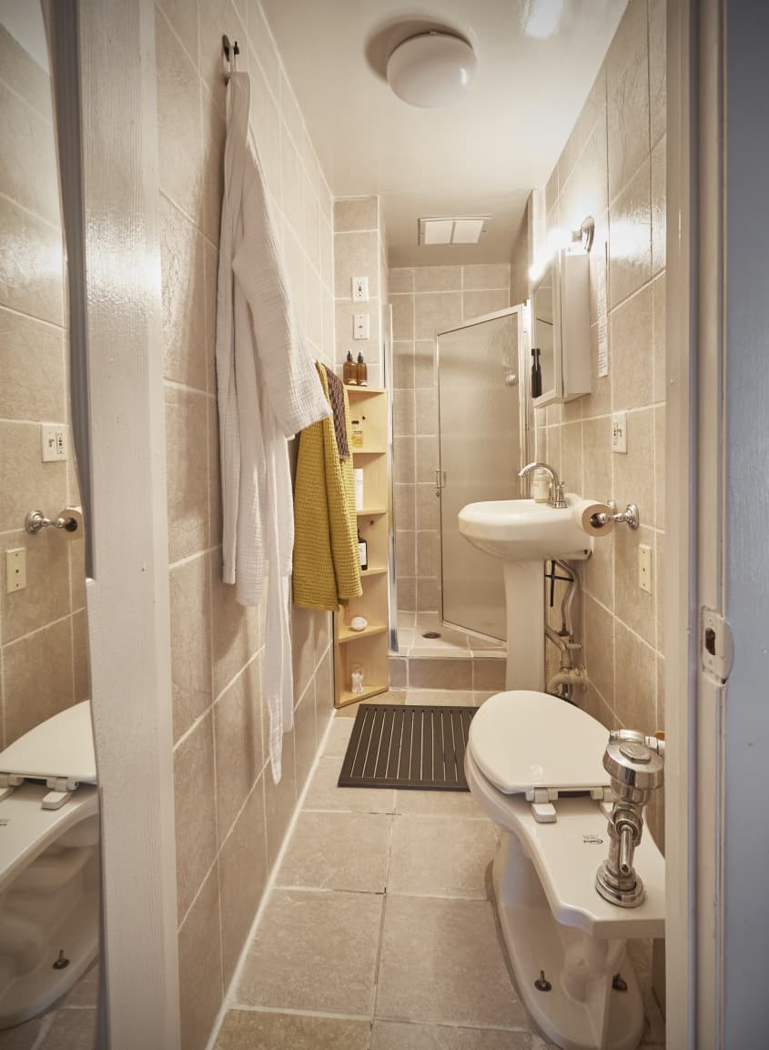 狭小的全米色瓷砖浴室，白色固定装置和侧卧厕所