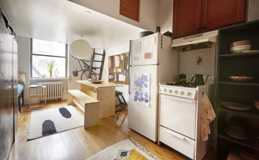 一个小工作室公寓的广角镜头，小厨房和大的天然木材餐桌和长凳