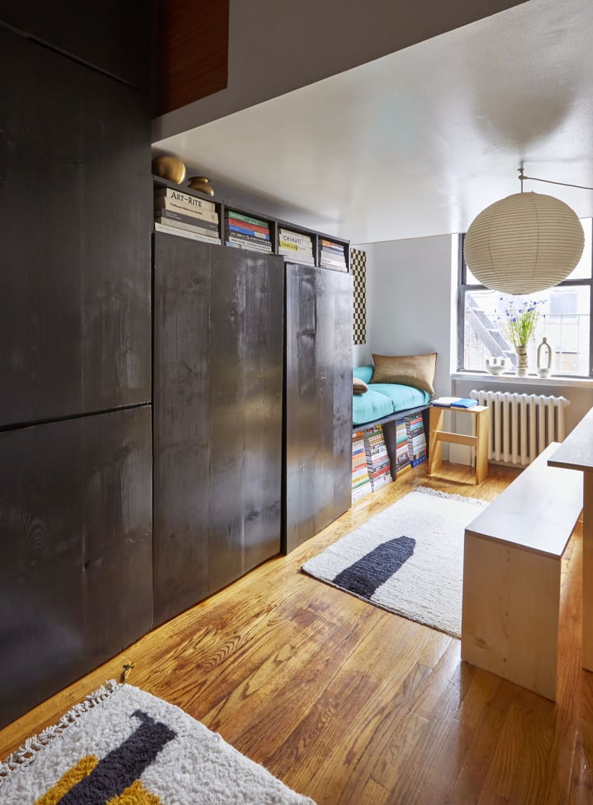 在一个小而有组织的现代一室公寓里，从地板到天花板的黑色DIY储物柜墙