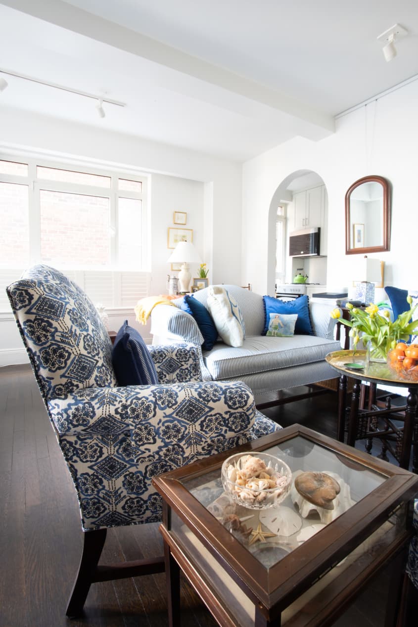 客厅有蓝色和白色图案的沙发和强调椅子，白色的墙壁，深色木地板。背景是拱形的门口