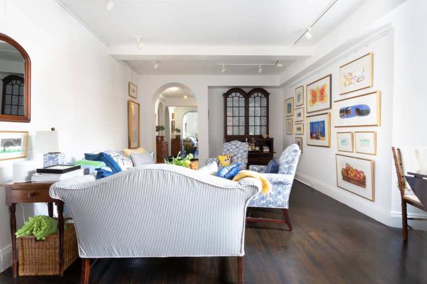 客厅有蓝色和白色图案的沙发和强调椅，白色墙壁，深色木地板和古董橱柜，也可以作为酒吧车。背景是拱形的门口