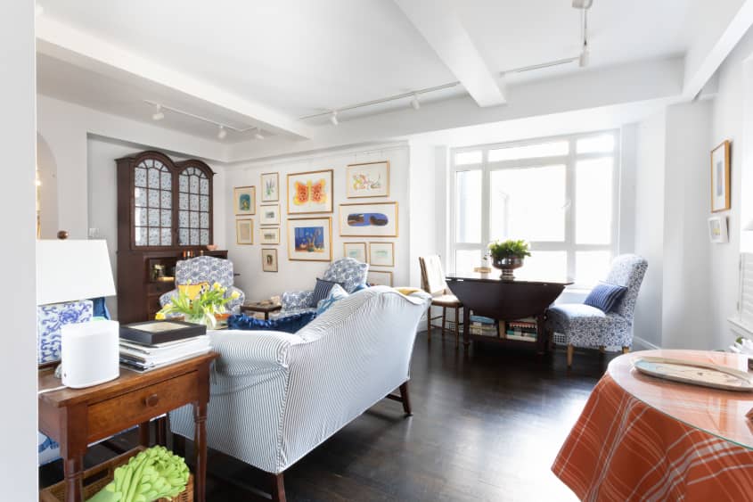 客厅有蓝色和白色图案的沙发和强调椅，白色墙壁，深色木地板和古董橱柜，也可以作为酒吧车。