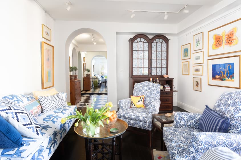 客厅有蓝色和白色图案的沙发和强调椅，白色墙壁，深色木地板和古董橱柜，也可以作为酒吧车