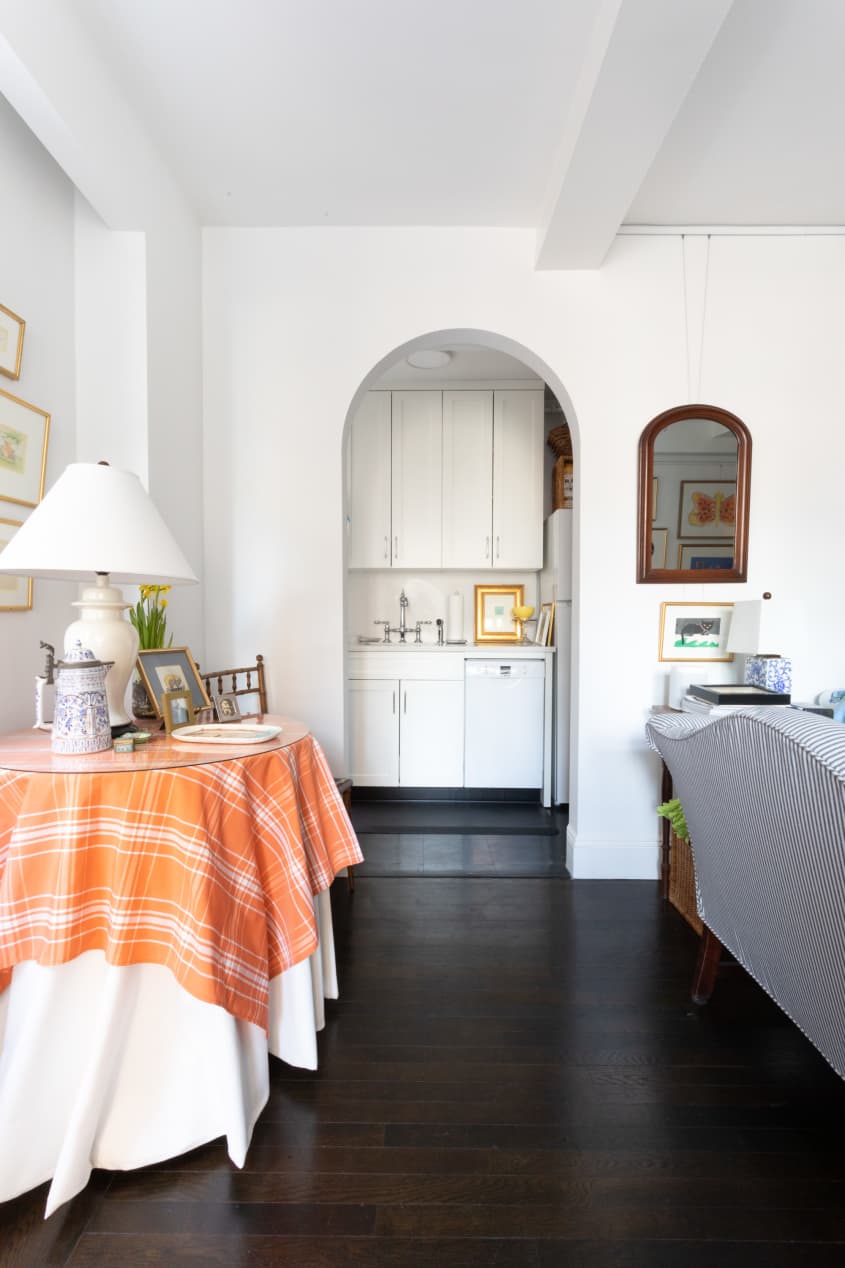 通往厨房的拱形门。前景有桌用橙白色桌布，白色台灯。沙发的背面可以看到在右边
