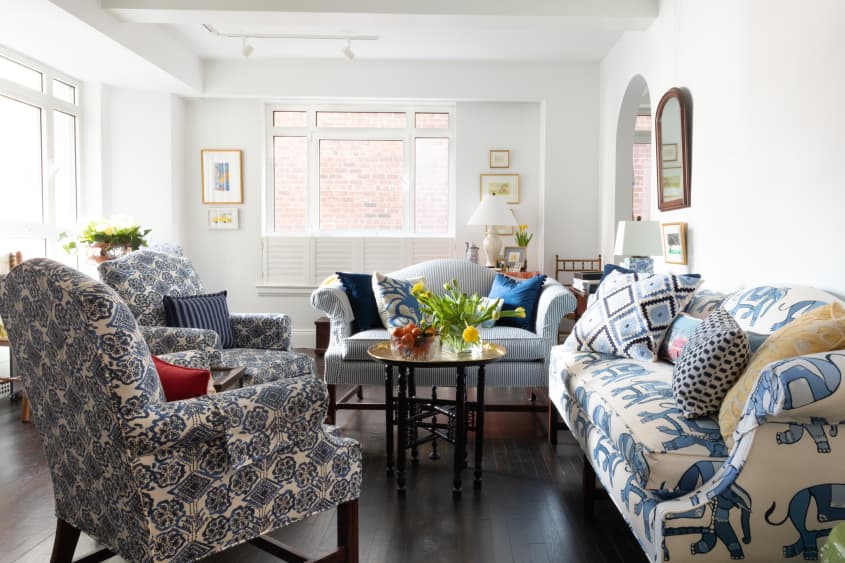 客厅有蓝色和白色图案的沙发和强调椅子，白色的墙壁，深色木地板。咖啡桌，花瓶里插着新鲜的郁金香