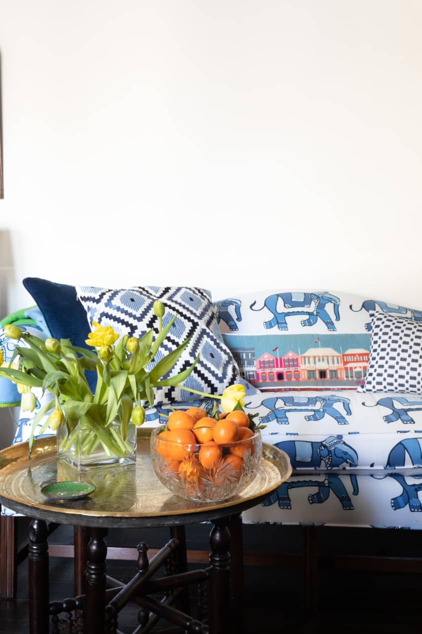 蓝色和白色图案沙发上的抱枕细节。咖啡桌上的圆托盘，花瓶里插着郁金香，玻璃碗里放着橘子