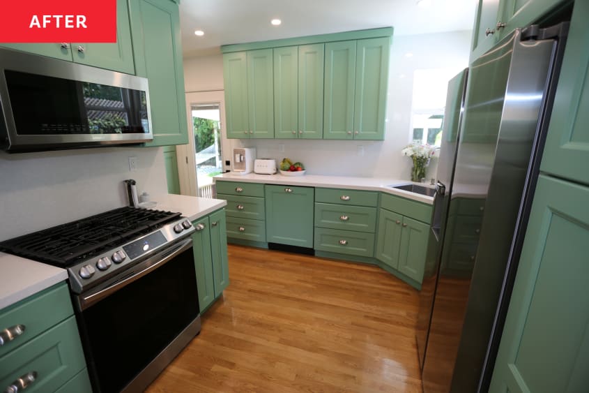 Green cabinets in newly renovated kitchen with stainless steel appliances and white stone countertops.