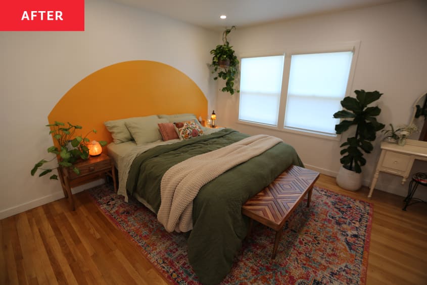 Yellow semi circle wall decal behind bed with neatly made bed green bedding. Wooden bench sits on foot end of bed in plant filled room.