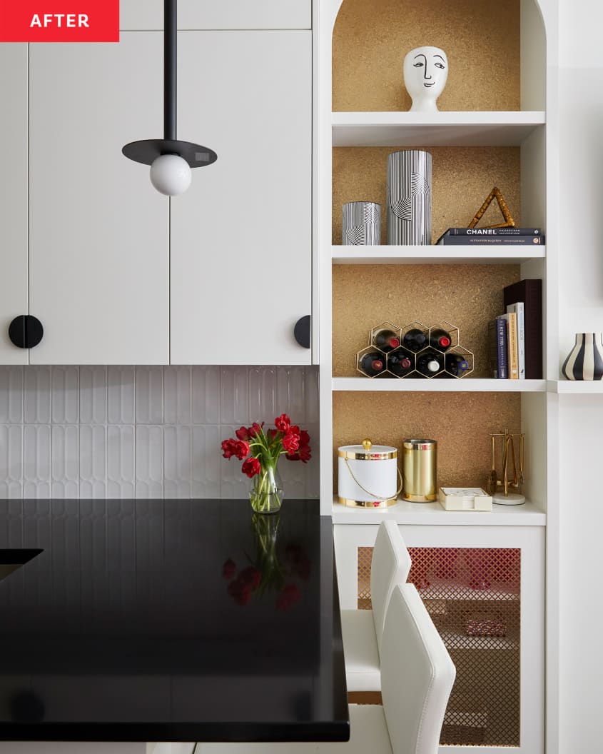 Gold-glitter wallpaper lines open shelves decorated with figurines and other objects. Black pendant lamp hangs over countertop with white stools underneath.