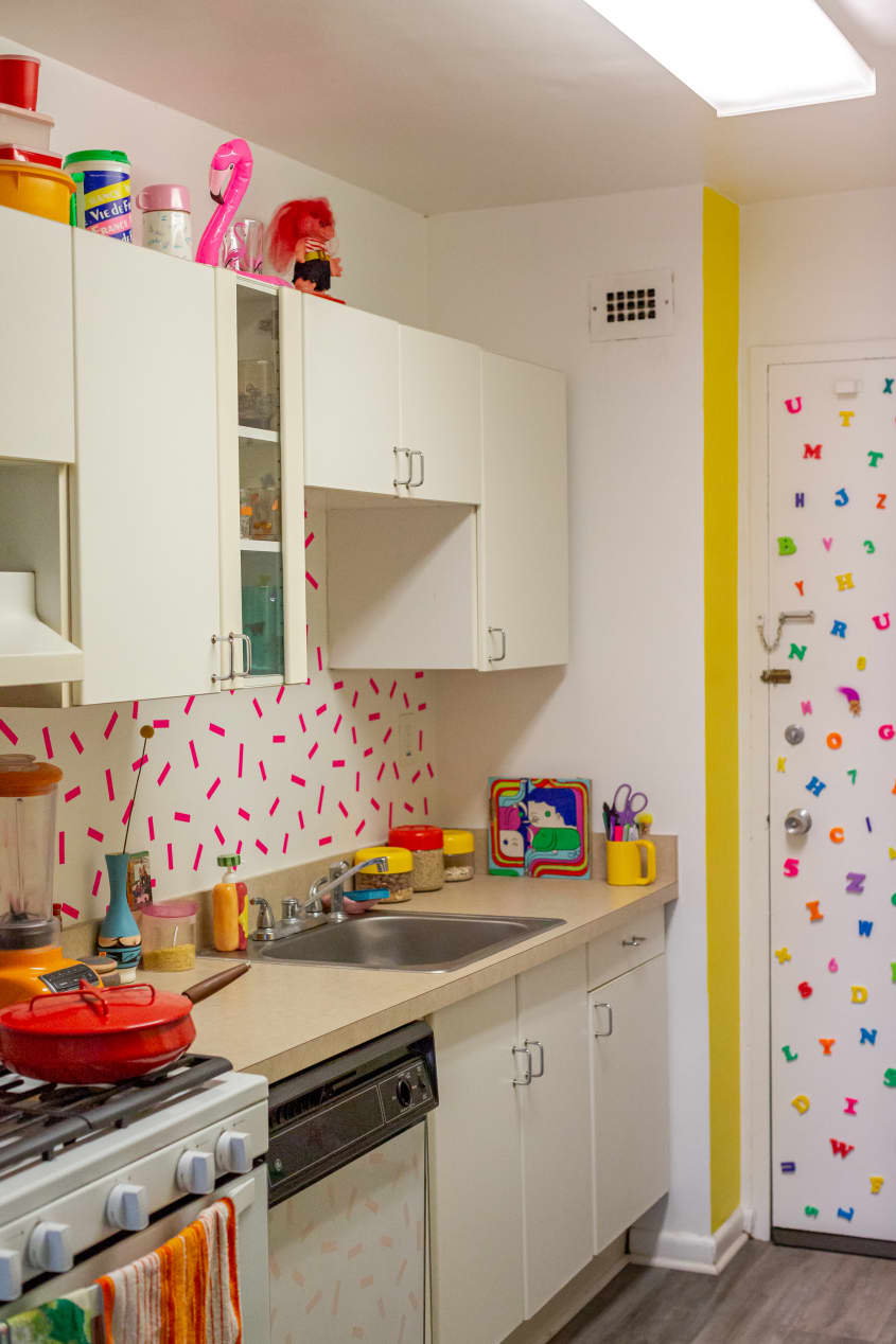 Kitchen with colorful patterned hot pink and white backsplash. White cabinets, colorful dishes and objects on stove and counter