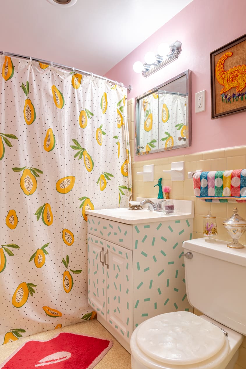Bathroom with lots of patterns on white. Pink painted walls, shower curtain with papaya design