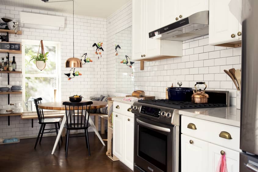 A white kitchen with floor-to-ceiling subway tiles and a small round kitchen table