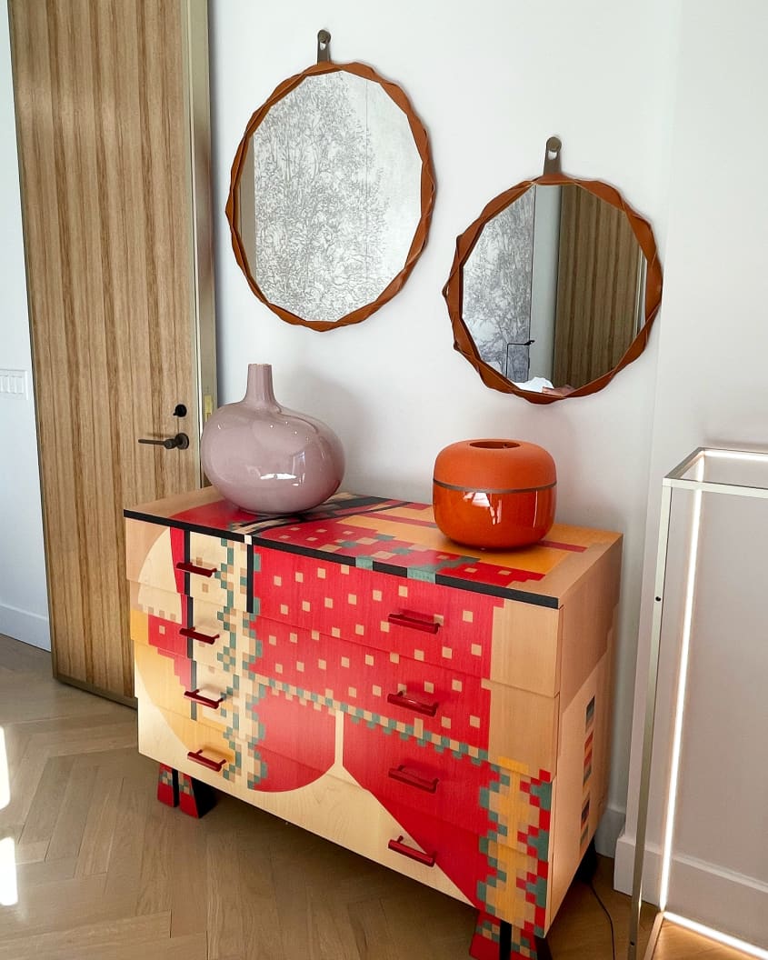 A red and tan dresser with two mirrors hanging above