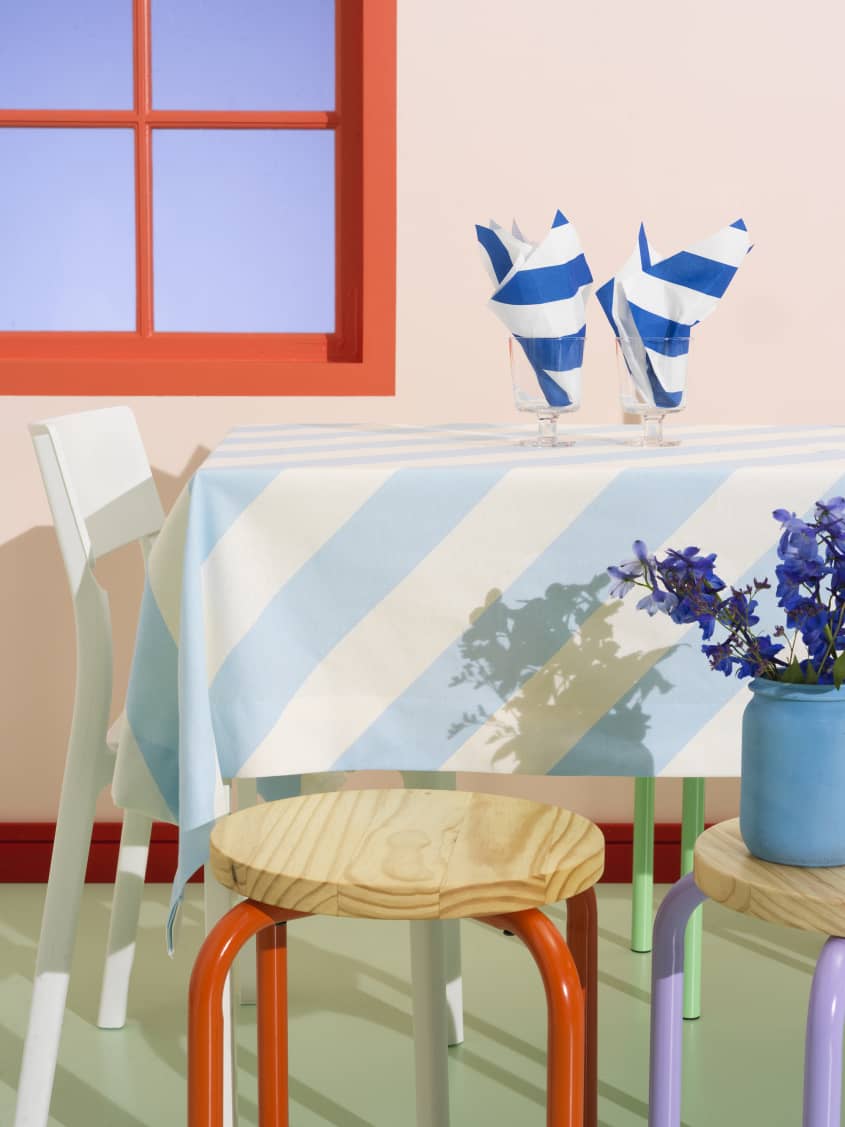 Colorful studio photo of items from the IKEA 80th anniversary Nytillverkad collection - table with blue and white striped tablecloth, striped napkins, stools with colorful legs