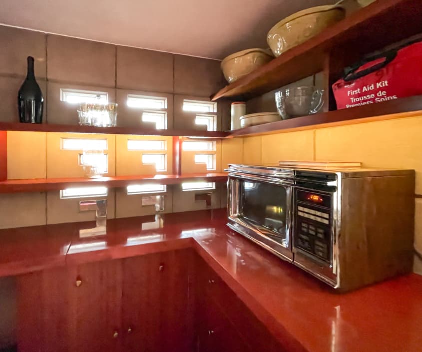 red wood counters and cabinets in a sleek kitchen with small cut out windows and old microwave