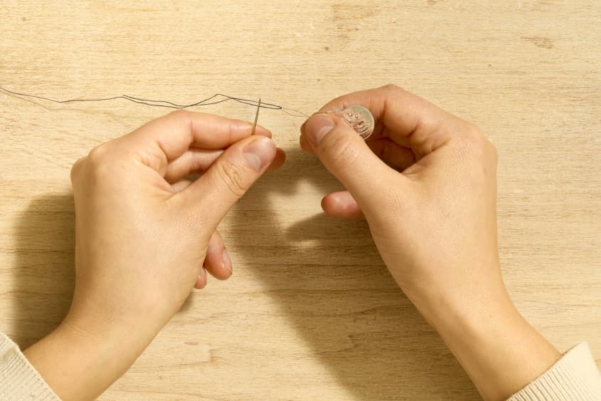 Overhead shot of two hands using a needle threader to thread a needle.