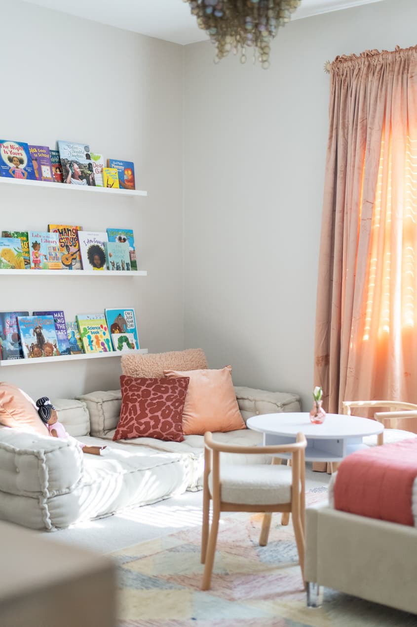 Kid's room designed by Marie Cloud of Indigo Pruitt with neutral furnishings and pops of coral and pink for contrast; view of reading area with floor cushions and shelf rails with books placed on them above it