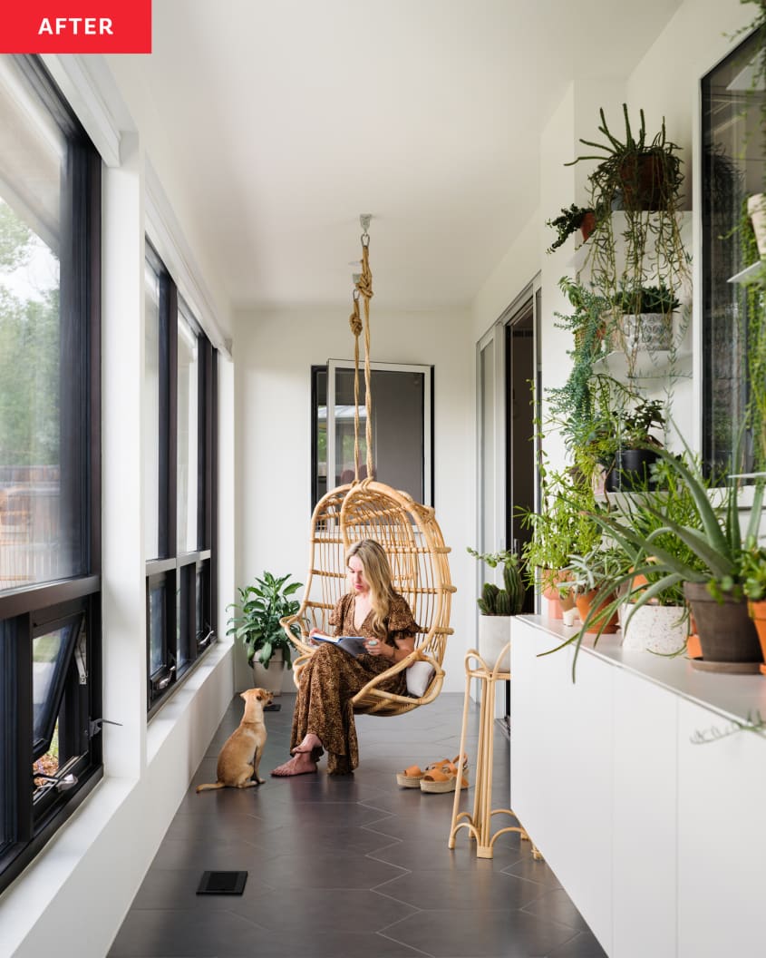 Hallway after renovation. Cane swing chair, large windows, shelf with lots of plants. Woman in chair with dog